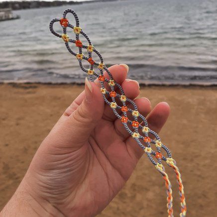 a hand holding up a string with beads on it near the water's edge