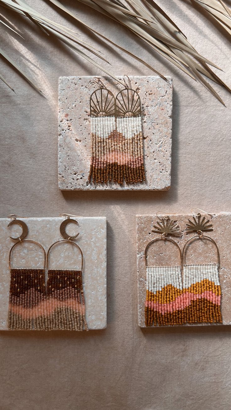 three small beaded earrings are hanging on the wall next to some palm fronds