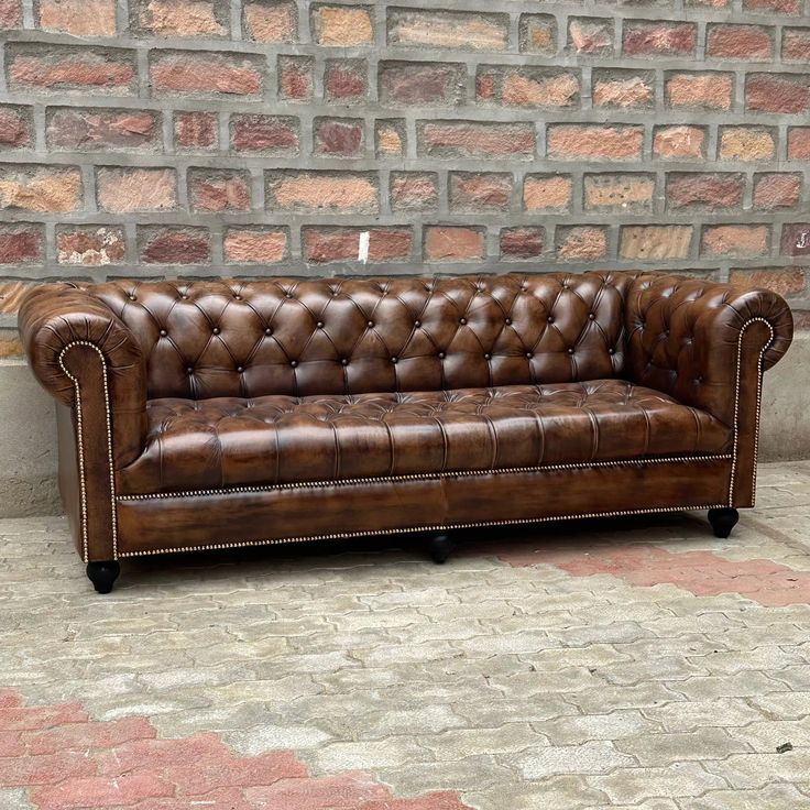 a brown leather couch sitting on top of a brick floor next to a stone wall