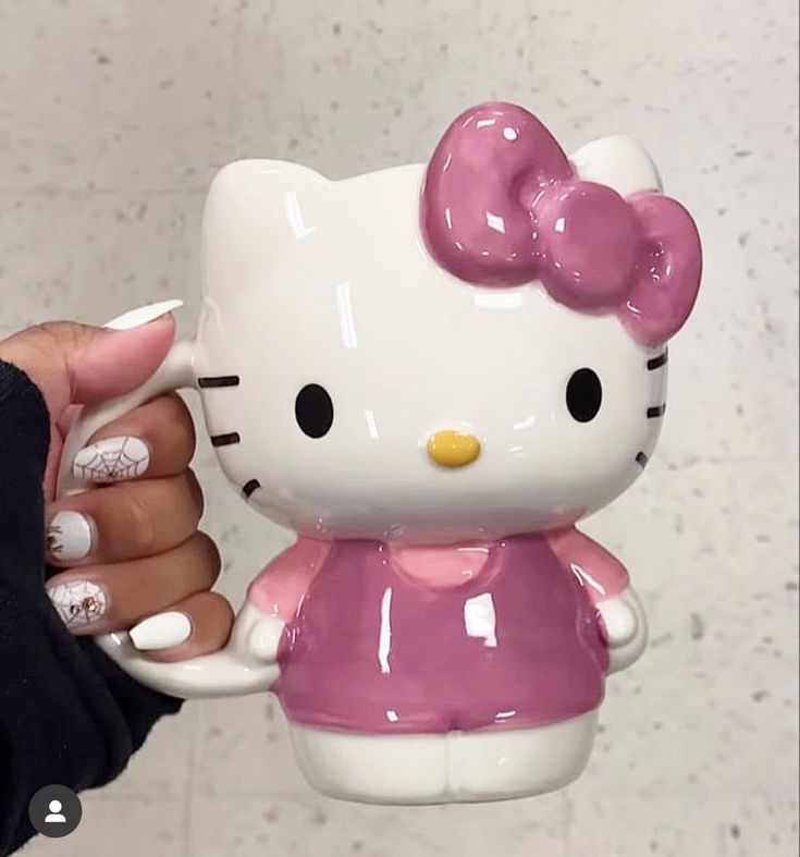 a hello kitty figurine is being held by a woman's hand in front of a wall