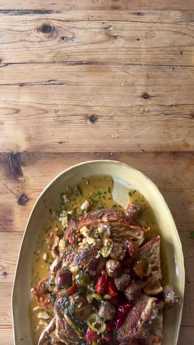 a white bowl filled with meat and vegetables on top of a wooden table next to a spoon