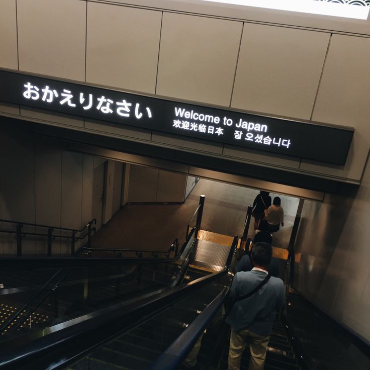 an escalator with people walking up and down it's rails in front of a sign that says welcome to japan