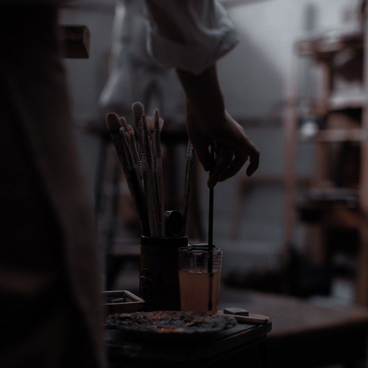 a person holding a paintbrush in front of a cup filled with brushes on top of a table