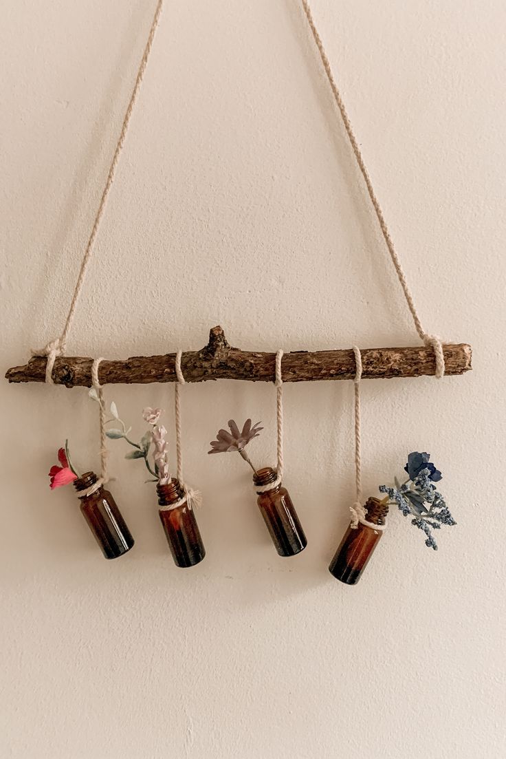 three bottles hanging from a wooden branch with flowers in them and some twine on the end