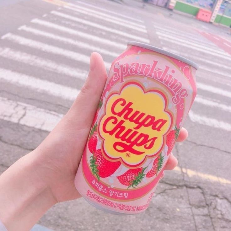 a person holding up a pink soda in front of a cross walk with the words chupa chups written on it