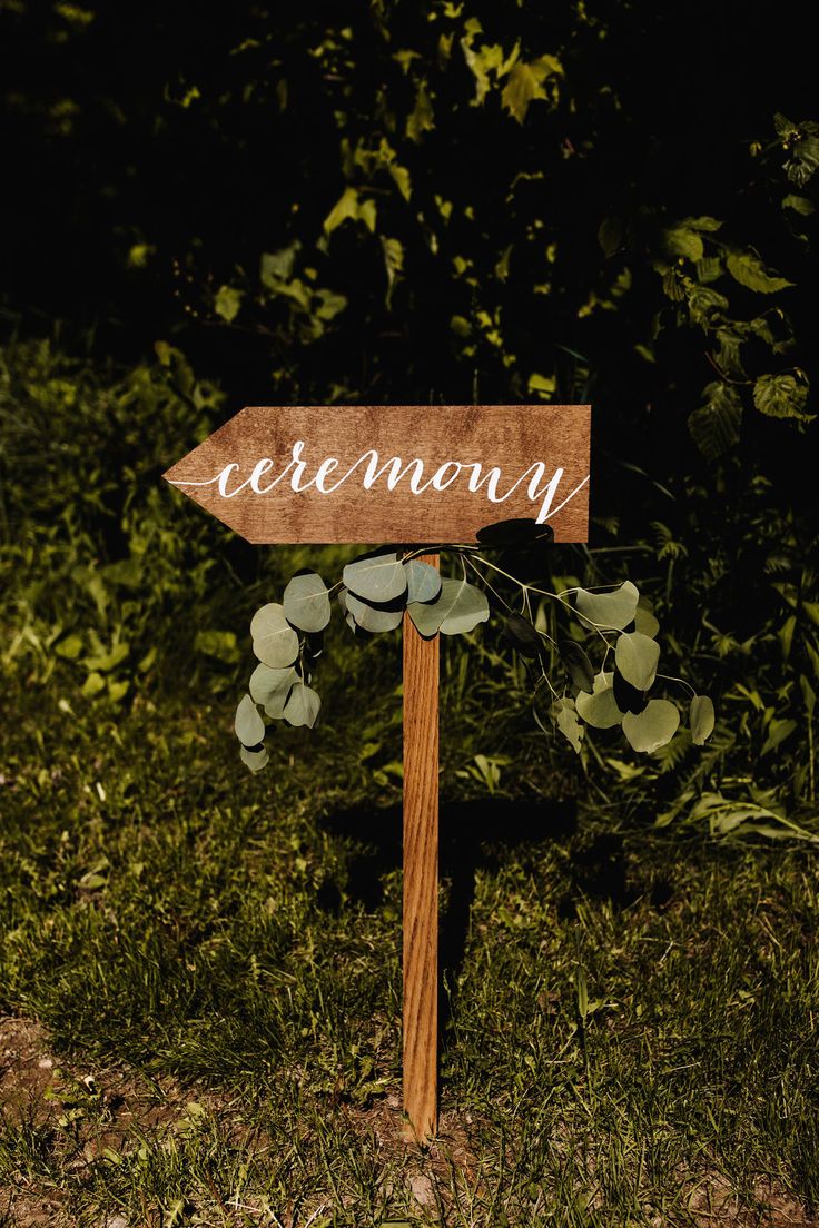 a wooden sign that says ceremony on it in front of some grass and bushes at night