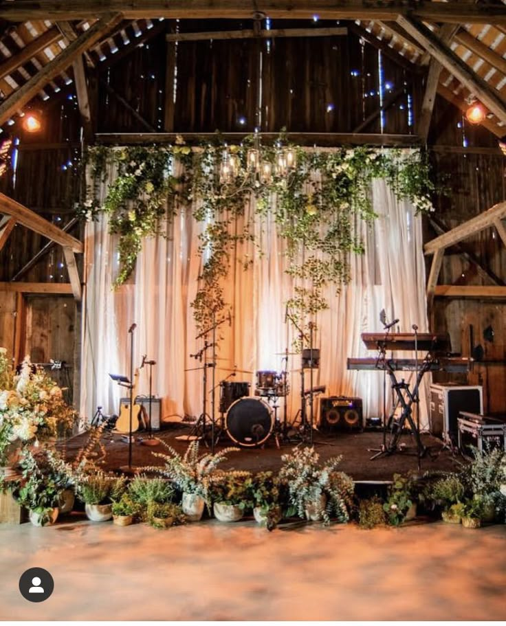 a stage set up for a wedding with greenery and lights on the ceiling, surrounded by potted plants