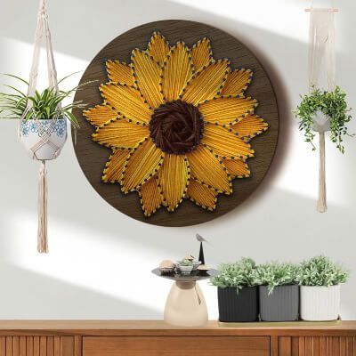 a sunflower made out of pasta hanging on the wall above a dresser with potted plants