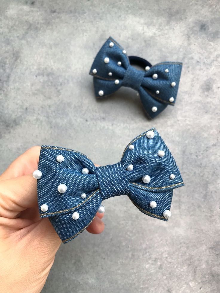 someone is holding two denim bows with white pearls on the ends and one in the middle