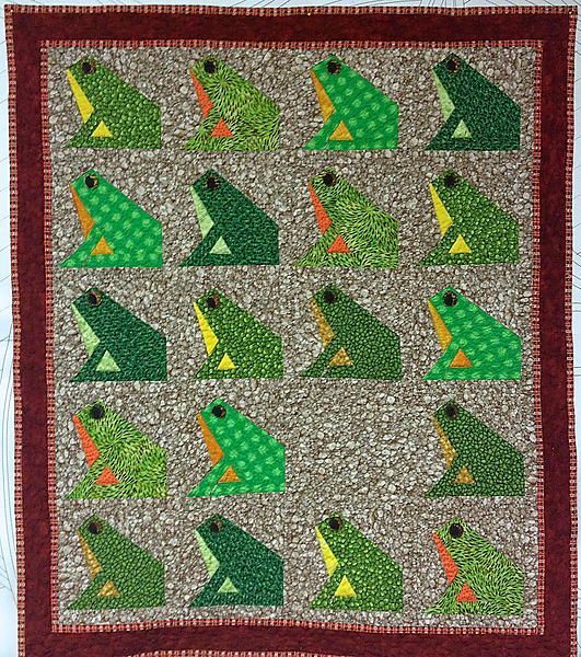 a quilted wall hanging with green frogs on it