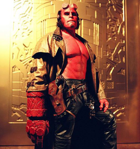 a man dressed as hellboy holding a large red object in his right hand and wearing leather pants