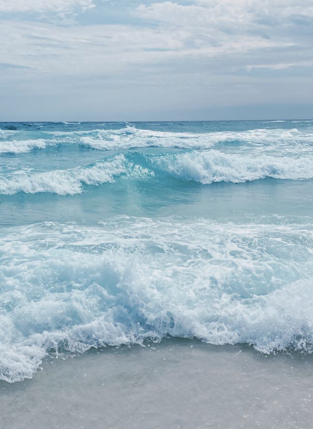 the ocean is blue and white with waves coming in from the shore on an overcast day