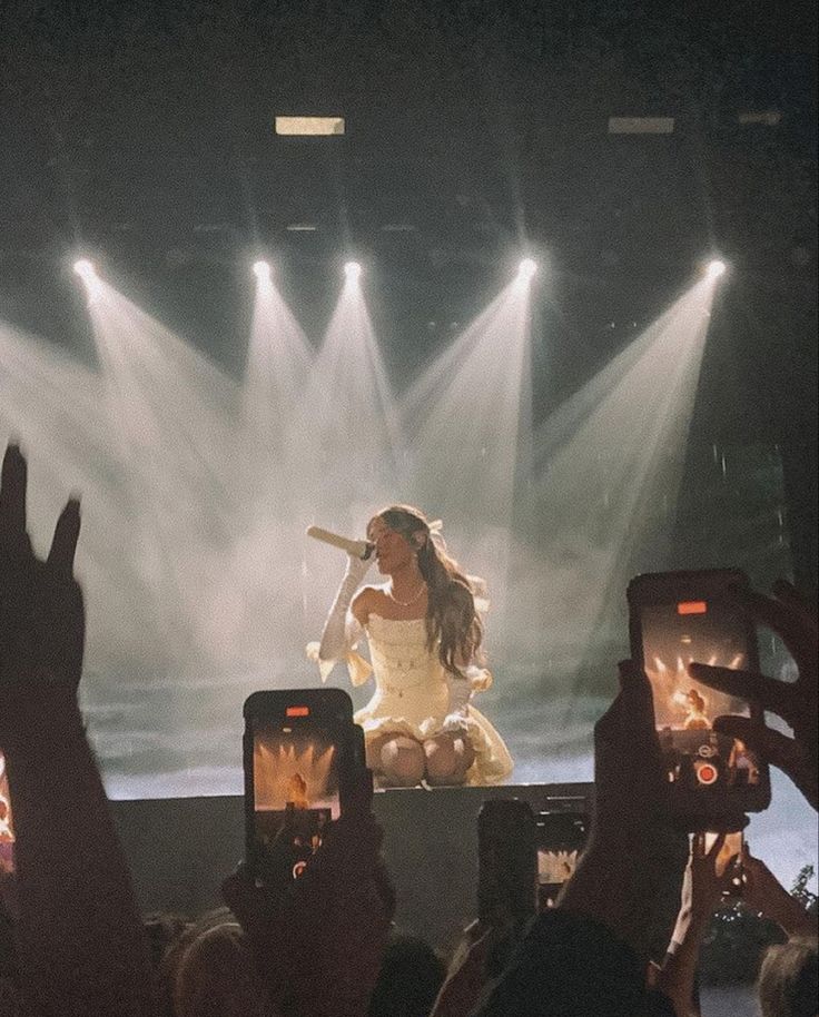 a woman in white dress on stage holding up her cell phone to take a photo