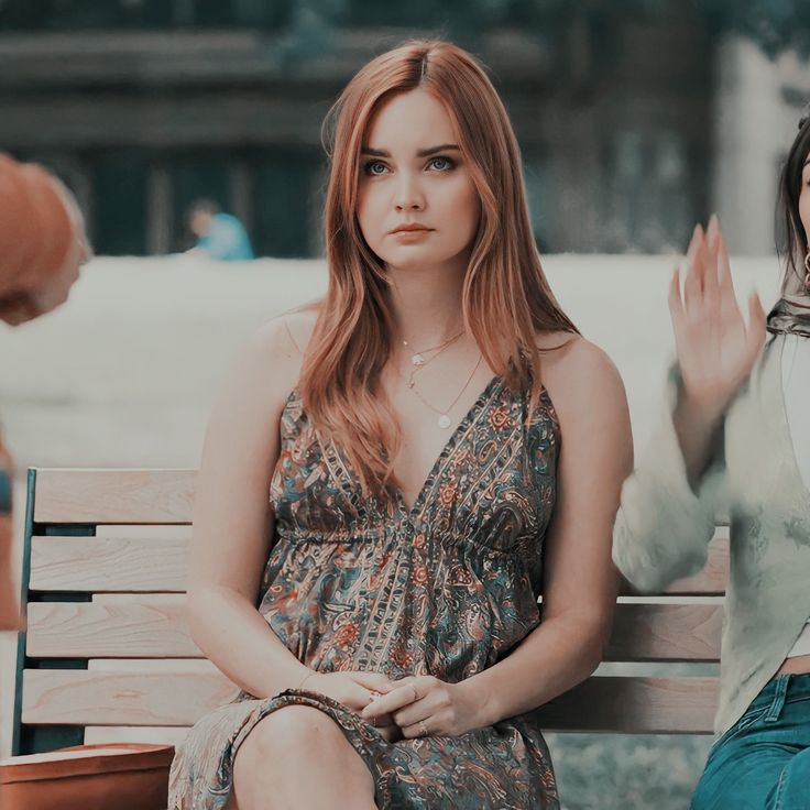 two women sitting on a wooden bench with their hands in the air and one holding her hand out