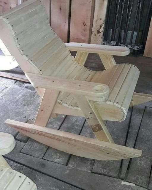 a wooden rocking chair sitting on top of a porch next to a fence and building materials