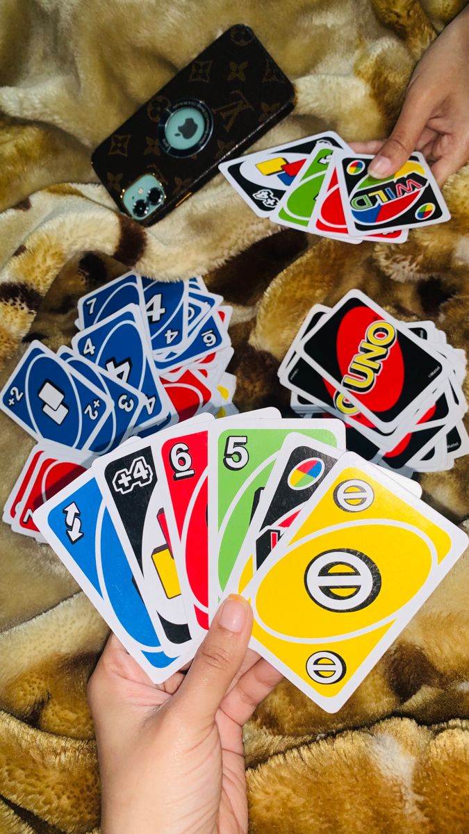 a person is holding playing cards in their hand while laying on a bed with a cell phone