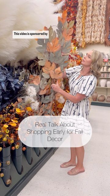 a woman standing in front of a display of fall leaves and other items with text overlay that reads real talk about shopping early for fall decor