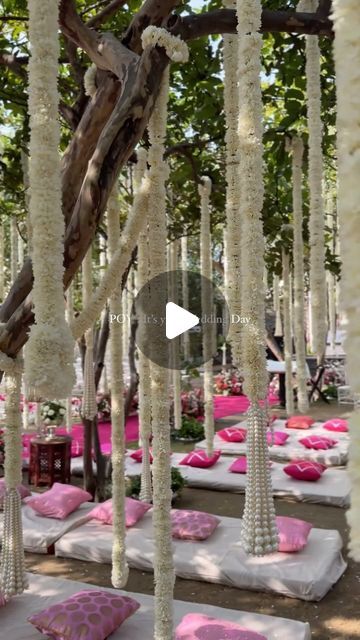 an outdoor ceremony setup with pink and white flowers on the ground, hanging from trees