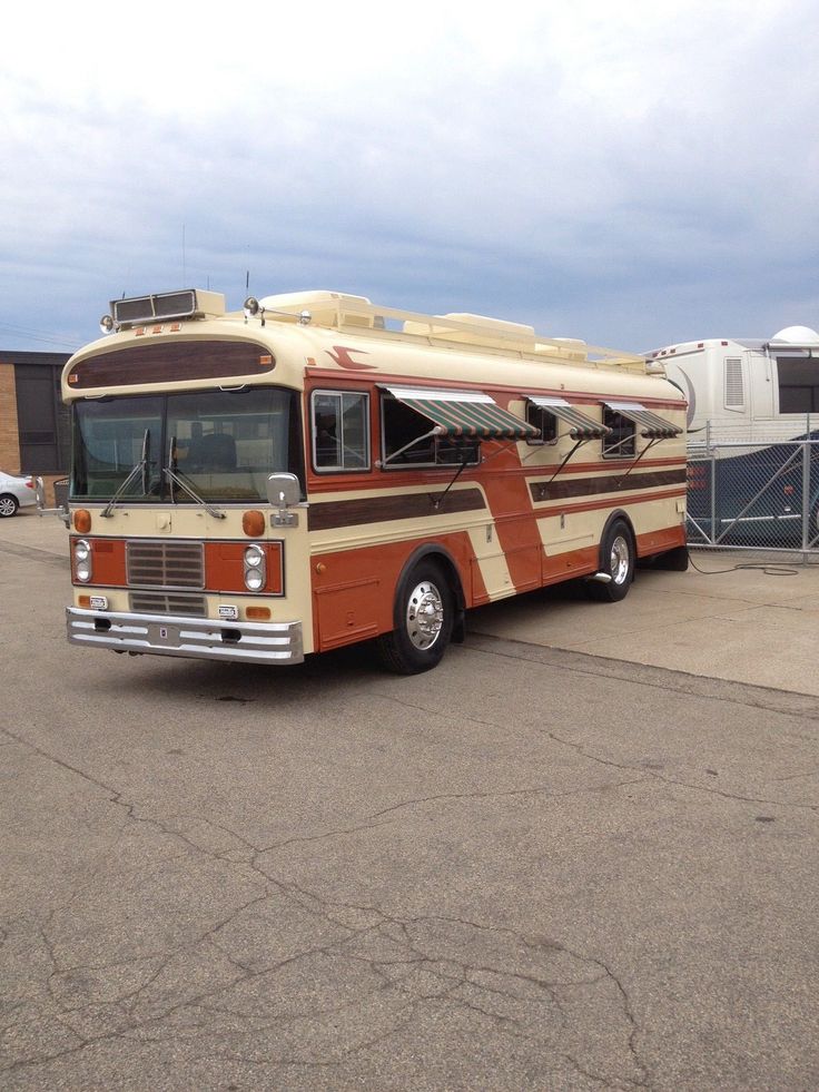 an orange and white bus parked in front of a building with other vehicles behind it