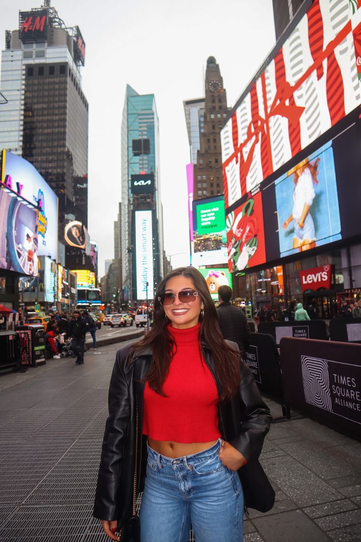 a woman standing in the middle of a city street wearing sunglasses and a red top