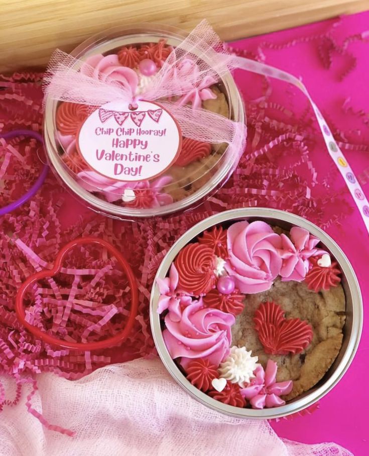 two tins filled with valentine's day cookies on top of a pink table cloth