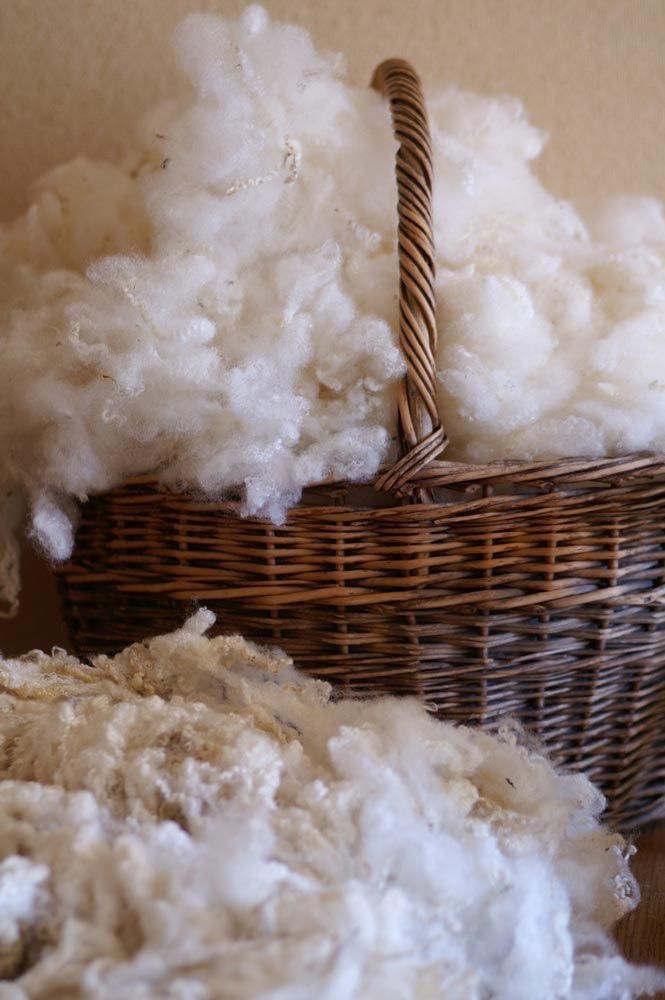 a basket filled with white fluffy next to a pile of wool