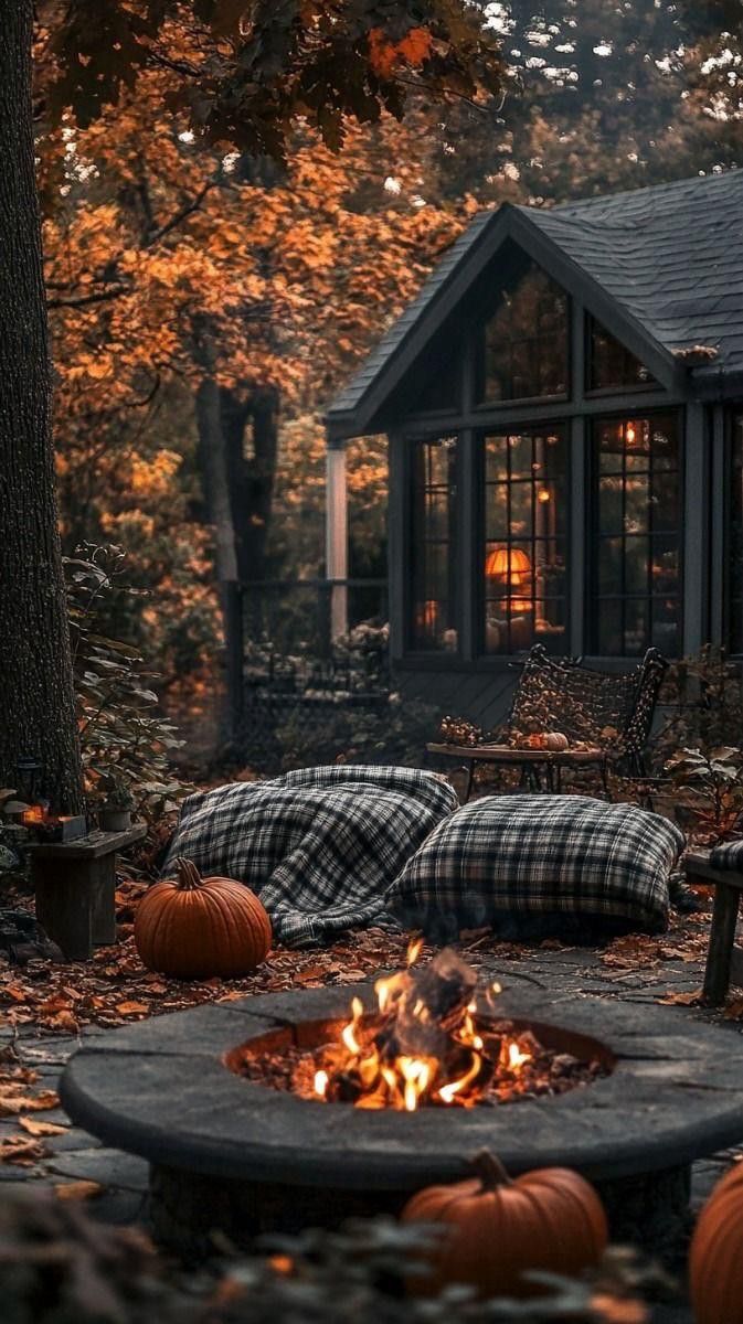 an outdoor fire pit with pumpkins around it in front of a cabin on a fall day