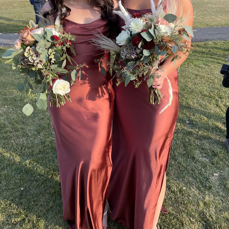 two bridesmaids in red dresses holding bouquets and posing for the camera at their wedding