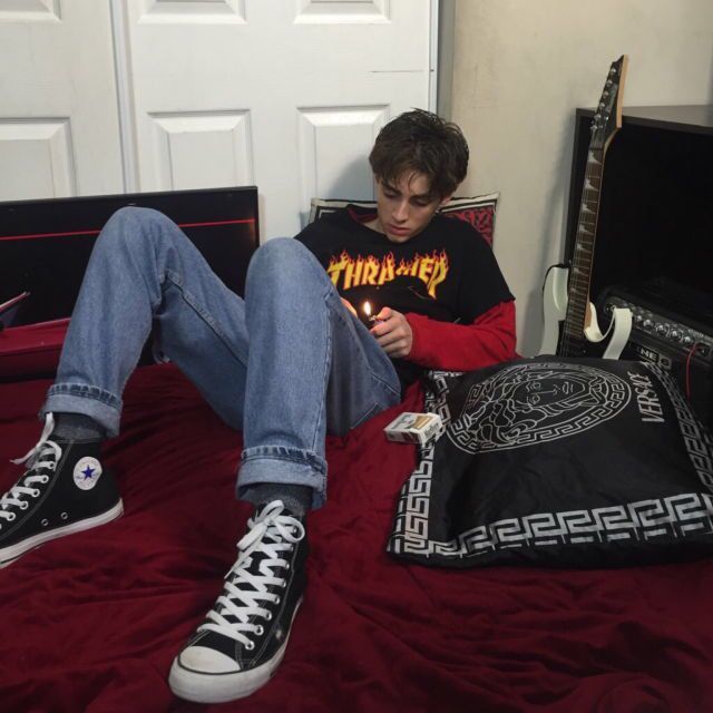 a young man sitting on top of a bed next to a guitar