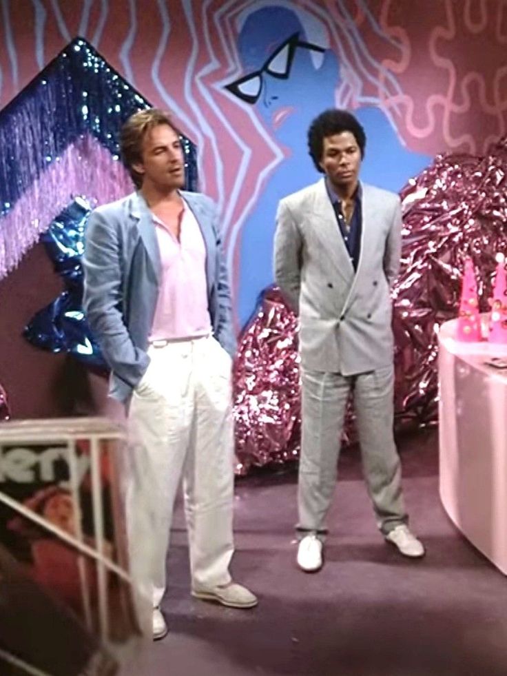 two men standing next to each other in front of a pink and purple wall with decorations on it