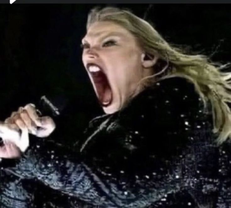 a woman singing into a microphone while holding her hands out in front of her face