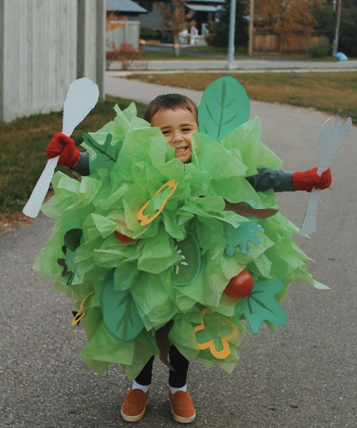 a young boy dressed up in a costume with green leaves and vegetables on his body