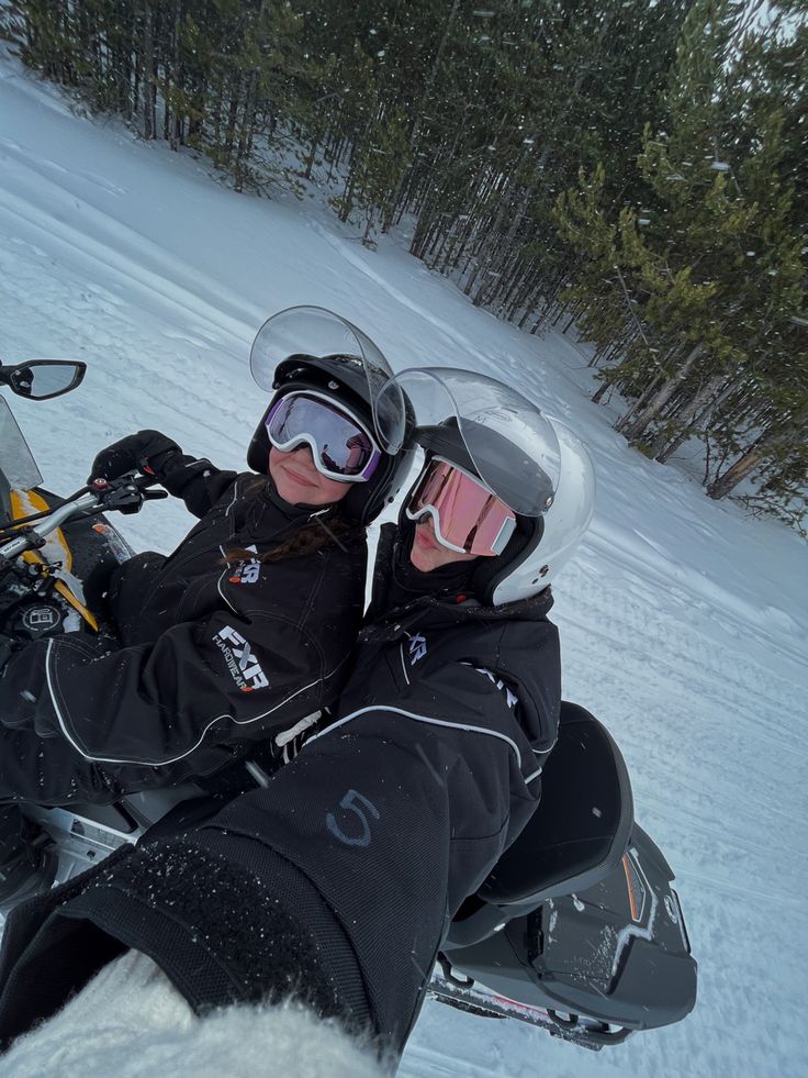 two people sitting in the snow with skis on their shoulders and one holding onto another person's back