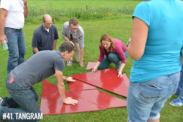 a group of people standing around a red object in the grass with one person reaching for it