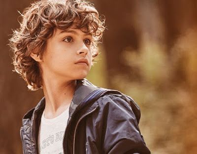 a young boy wearing a black jacket and white t - shirt looking off into the distance