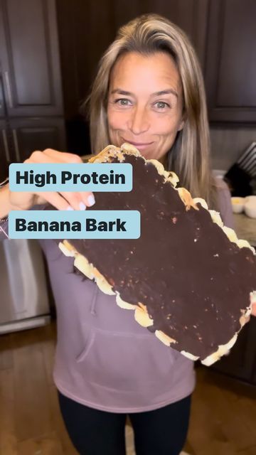 a woman holding up a large piece of chocolate in her hands with the words high protein banana bark on it