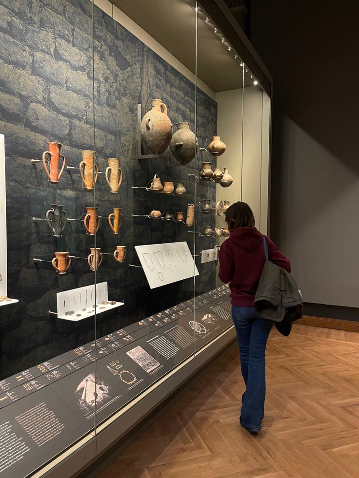 a woman looking at vases on display in a museum