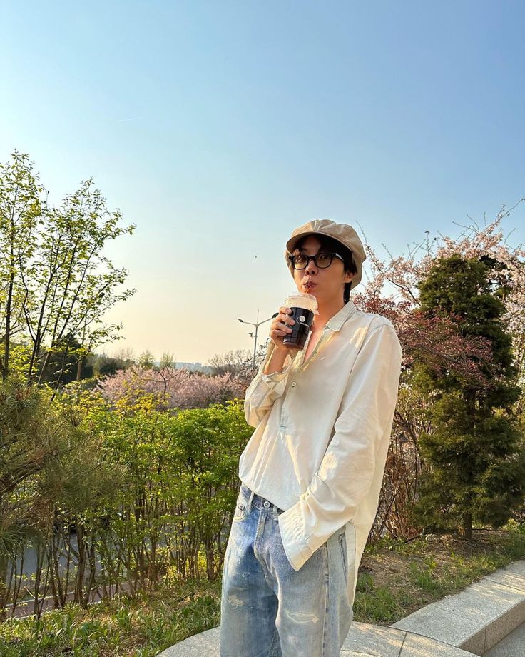 a woman standing on the side of a road holding a coffee cup in her hand