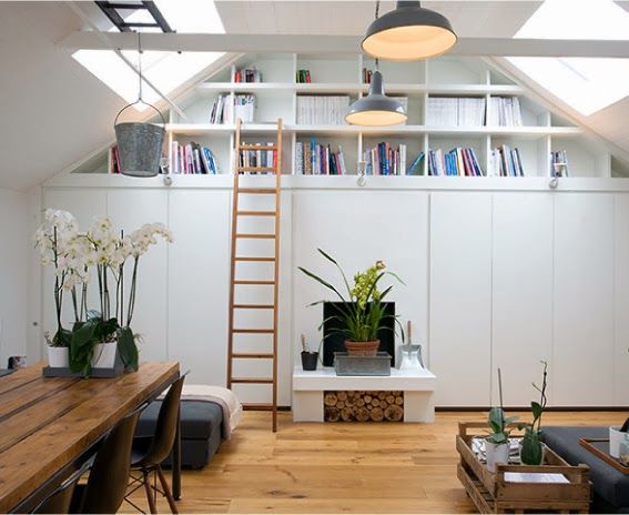 a loft apartment with white walls and wooden flooring is decorated with plants, bookshelves, and ladder to the ceiling