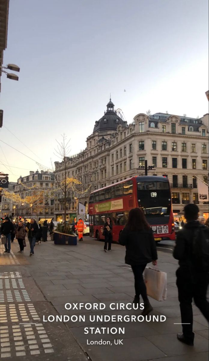 people are walking on the sidewalk in front of some buildings and two red double decker buses