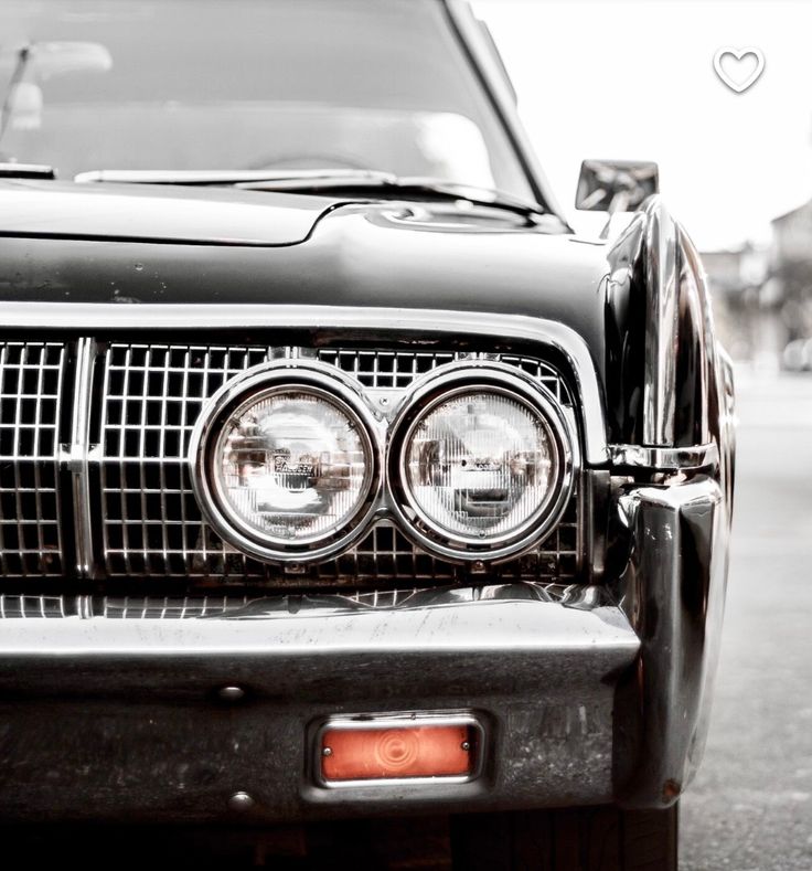 the front end of an old black car with its lights turned on and it's grill missing