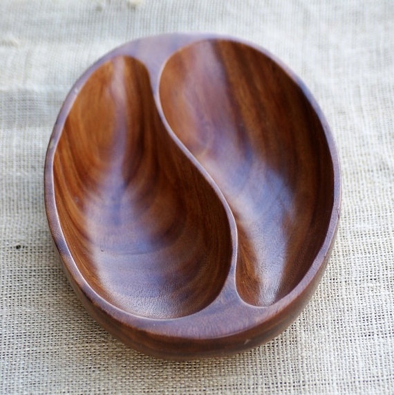 a wooden bowl sitting on top of a cloth covered tablecloth with two spoons in it