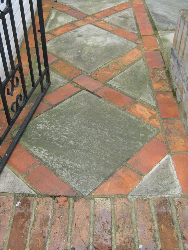 an iron gate on the side of a brick walkway with red and green tiles around it