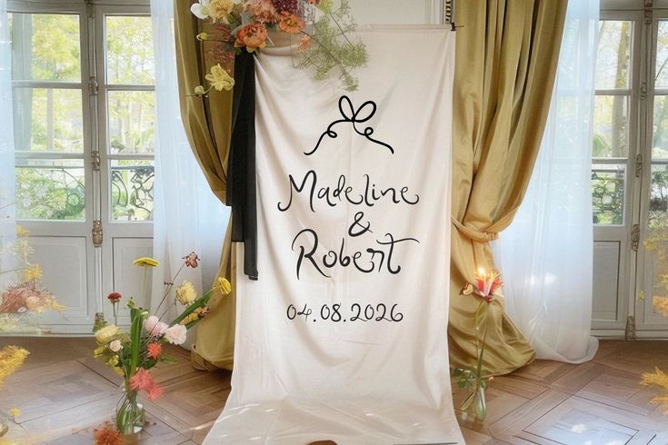 a wedding ceremony backdrop with flowers and candles in front of the curtained room windows