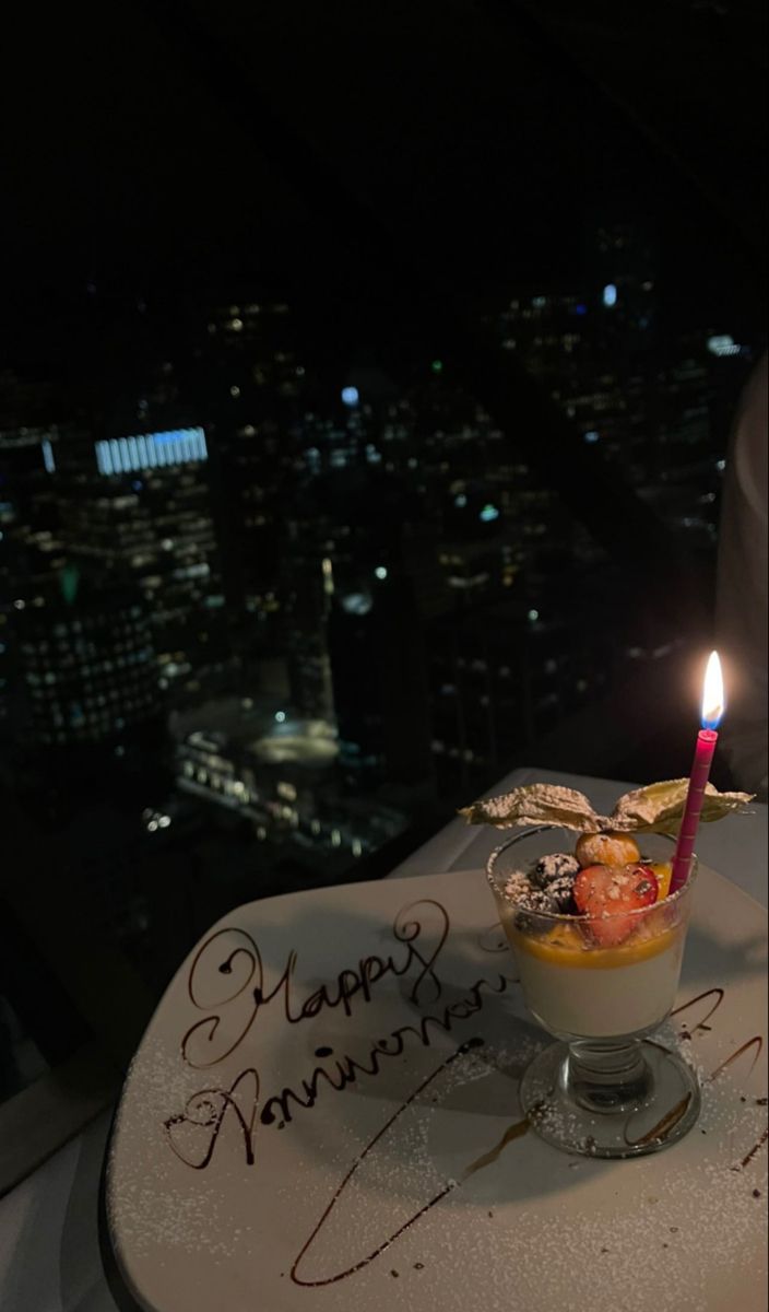 a birthday cake with a candle on top of it in front of a cityscape