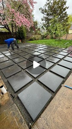 a man is working on an outdoor area with black tiles and a dog standing next to it