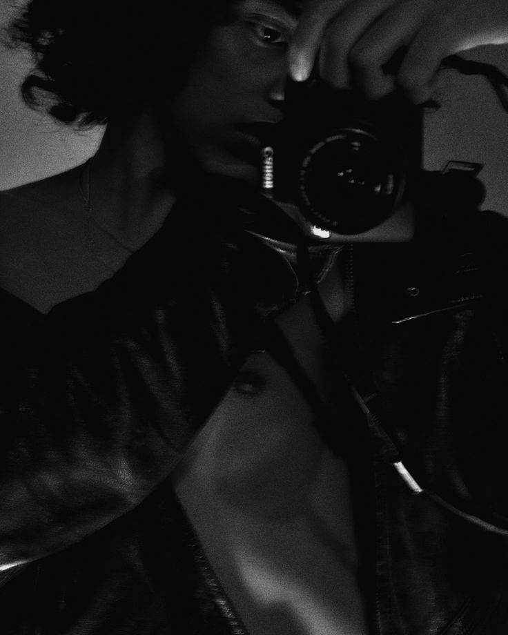 black and white photograph of a woman holding a camera to her face while wearing a leather jacket