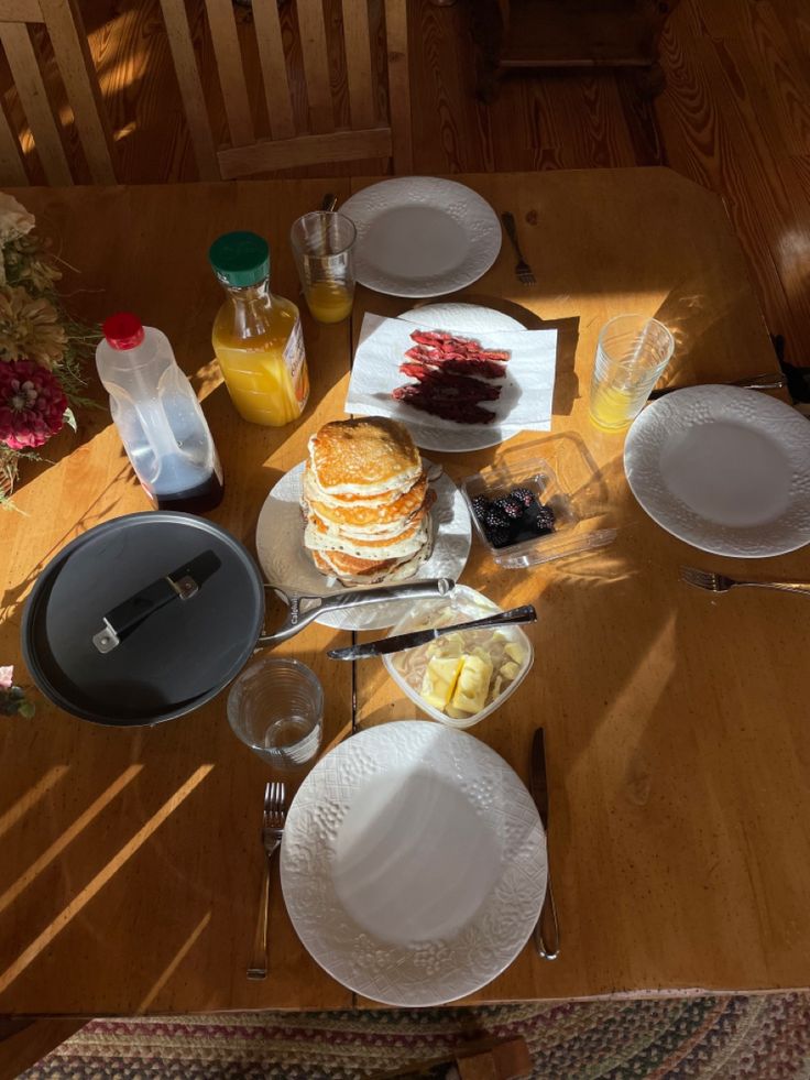 a wooden table topped with white plates and dishes covered in cake next to bottles of orange juice