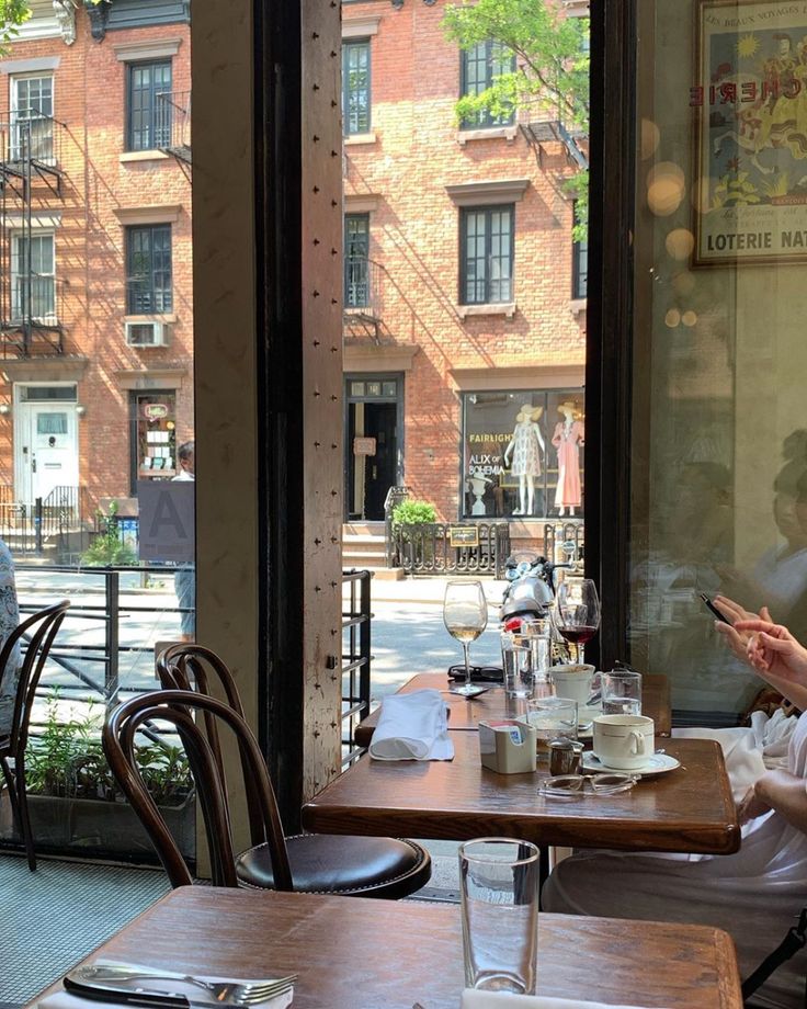 a woman sitting at a table in front of a window looking at her cell phone