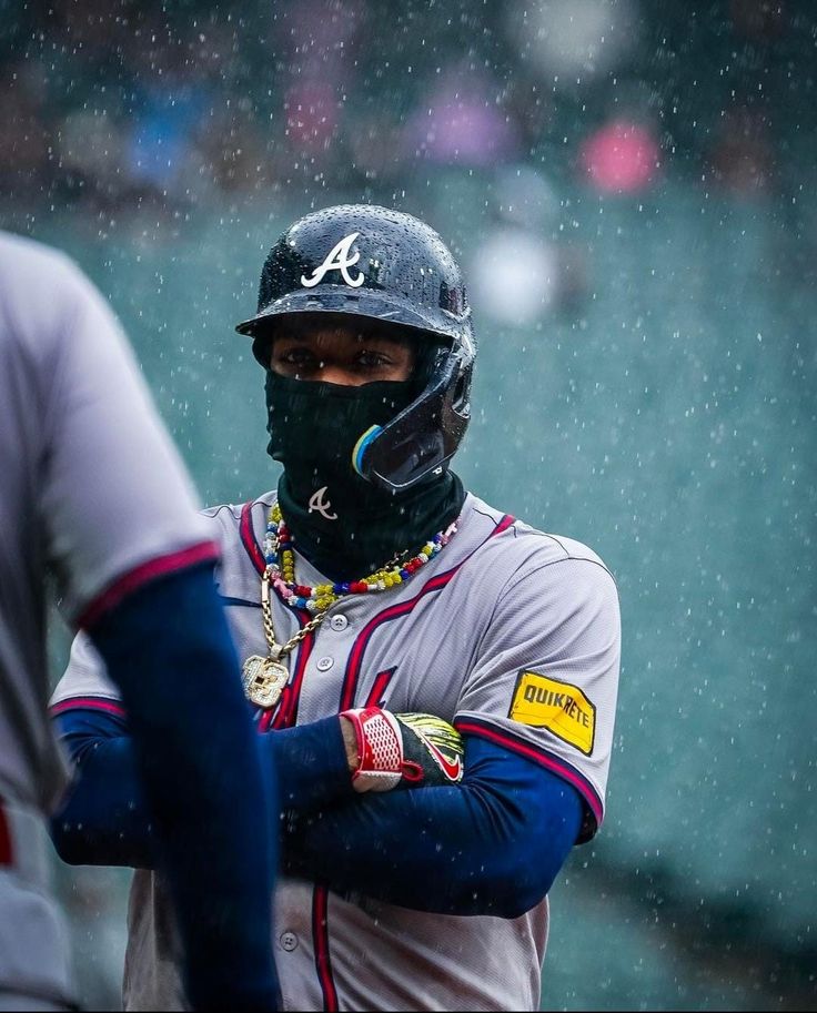 a baseball player wearing a face mask and holding his hands on his chest in the rain